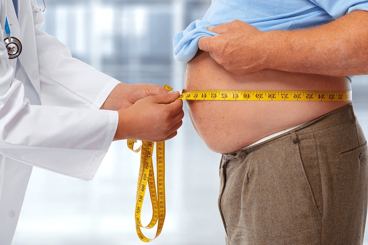 Läkare mäter omkretsen med måttband av magen på en överviktig man. 
